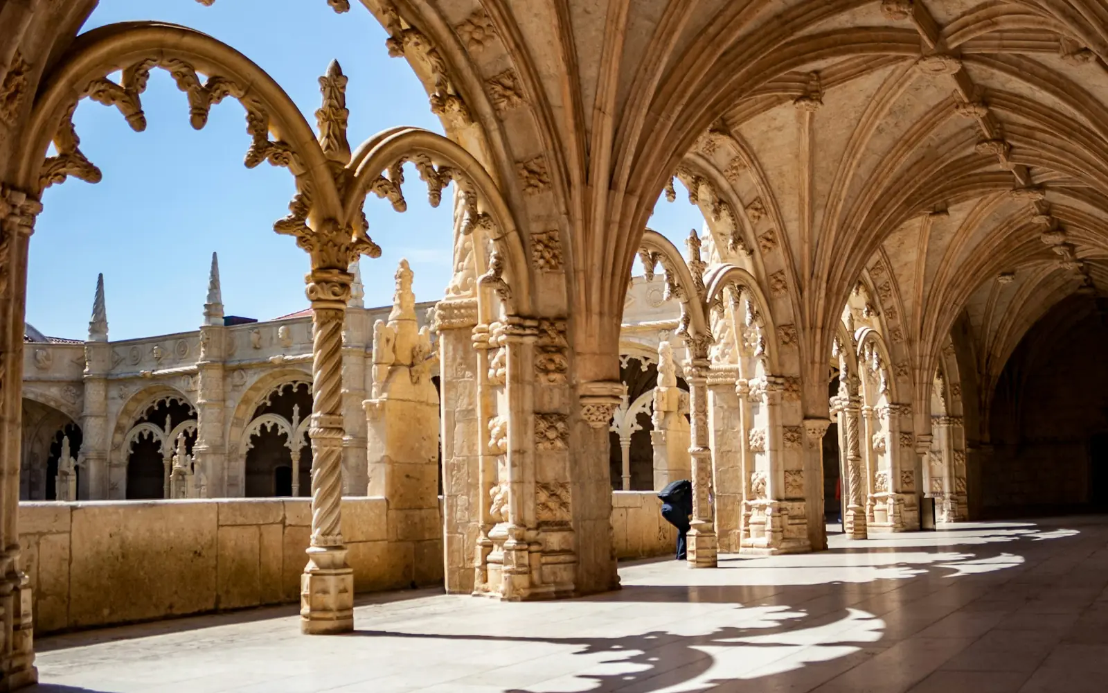 Sunlight through the lower cloister arcade of the Jerónimos Monastery, tracery casting shadows on the stone floor